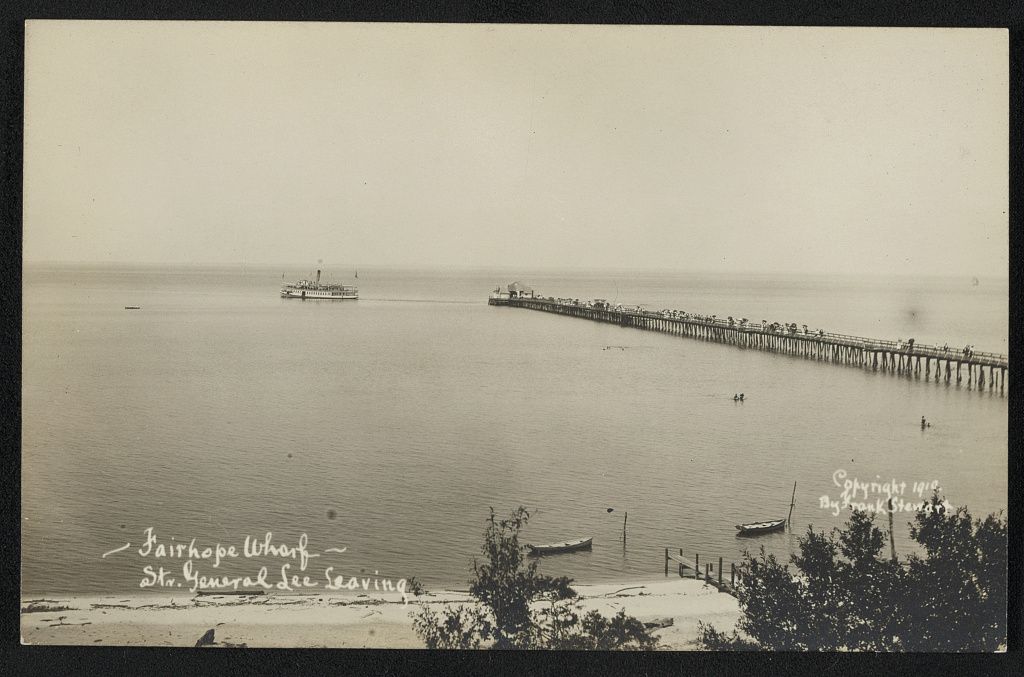 Sepia photo postcard of a long wooden pier running out into the bay at Fairhope, Alabama, with a steamboat pulling away